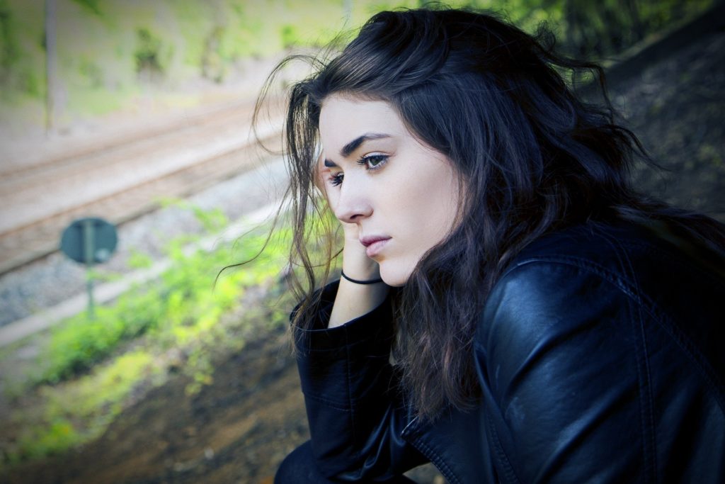 woman in a leather jacket sitting down resting her hand on her face while she looks out into the distance
